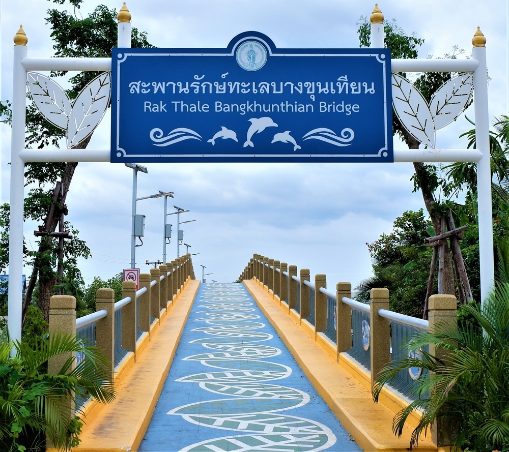 ป้าย "สะพานรักทะเลบางขุนเทียน" เป็นภาษาไทยและอังกฤษแสดงอยู่ที่ทางเข้า สถานที่ฮันนีมูนในไทย สะพานคนเดินสีน้ำเงินที่ประดับด้วยลวดลายทะเลและล้อมรอบด้วยพันธุ์ไม้เมืองร้อน ทำให้เป็นสถานที่ในอุดมคติของโฮนีมูนในไทย