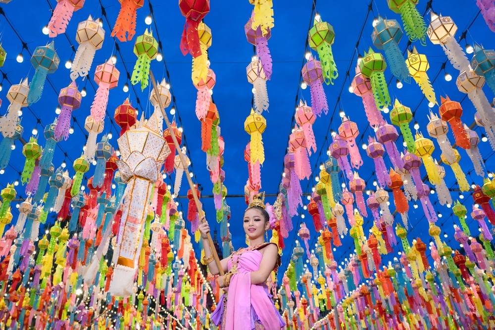 คนในชุดพื้นเมืองถือโคมไฟท่ามกลางโคมไฟแขวนหลากสีสันในงานเทศกาลงานลอยกระทงในช่วงเย็น