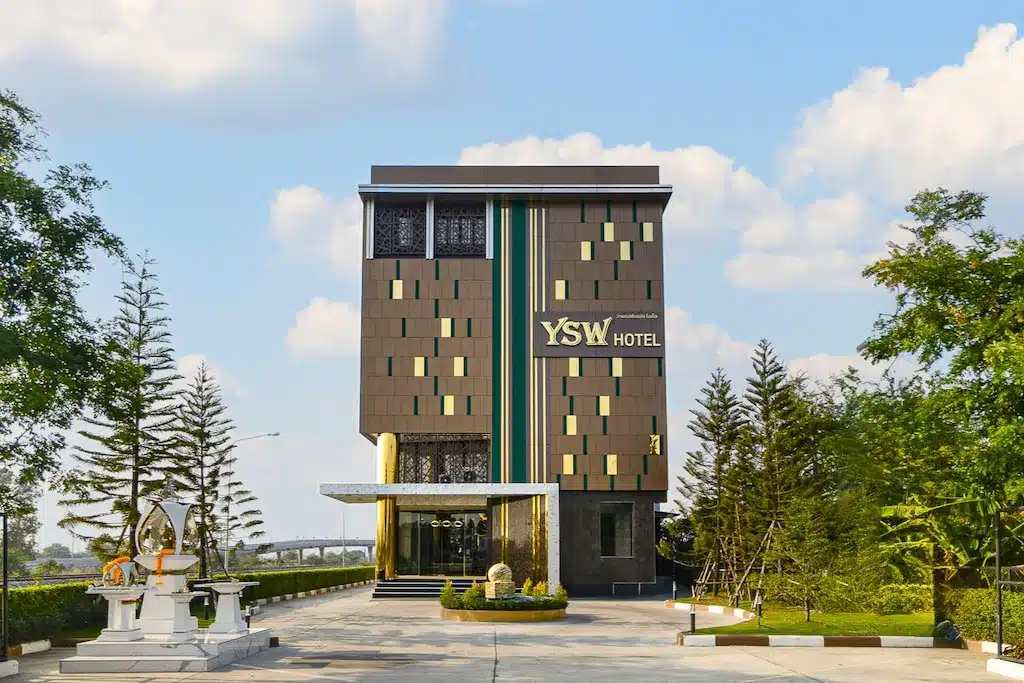 อาคารโรงแรมทันสมัยหลายชั้นที่มีป้าย "YSW Hotel" บนด้านหน้า ล้อมรอบด้วยภูมิทัศน์อันเขียวขจีอย่างประณีตและมีทางเดินหินที่ทอดไปสู่ทางเข้า ถือเป็นที่เที่ยวหน้าฝนโรแมนติกที่สมบูรณ์แบบ จังหวัดเมืองรอง