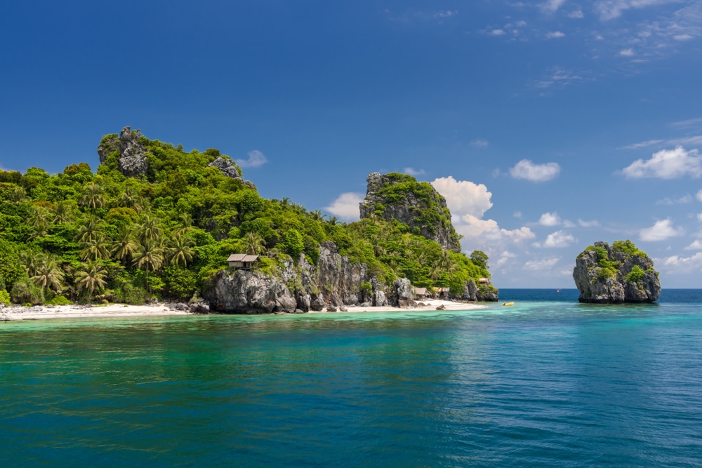 เกาะเขตร้อนที่มีต้นไม้เขียวขจีและหินเรียงตามหาดทรายขาว ล้อมรอบด้วยมหาสมุทรสีฟ้าใสภายใต้ท้องฟ้าที่มีเมฆบางส่วน ถือเป็นสถานที่เที่ยวหน้าฝนโรแมนติกสำหรับคู่รักที่กำลังมองหาสถานที่พักผ่อนอันเงียบสงบอย่างแท้จริง เมืองรองน่าเที่ยว"