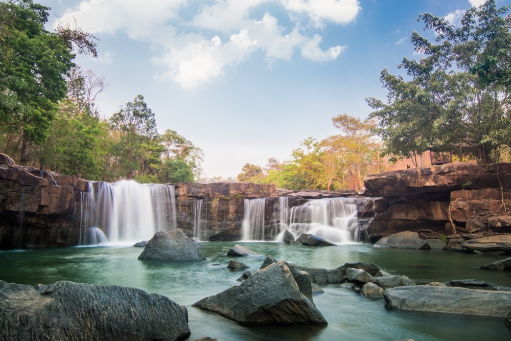 น้ำตกอันเงียบสงบที่รู้จักกันในชื่อ น้ำตกที่สวยที่สุดในประเทศไทย น้ำตกในประเทศไทยในประเทศไทย มีน้ำตกไหลผ่านโขดหินลงสู่แอ่งน้ำอันเงียบสงบ ล้อมรอบด้วยต้นไม้สีเขียวชอุ่มและท้องฟ้าแจ่มใสและมีเมฆบางส่วน