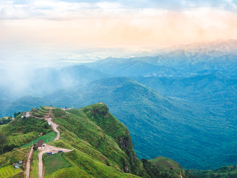 สัมผัสทัศนียภาพอันงดงามของทิวเขาเขียวขจีที่มีทางเดินคดเคี้ยว บ้านเรือน และเส้นขอบฟ้าอันกว้างใหญ่ภายใต้ท้องฟ้าที่มีเมฆบางส่วน เหมาะสำหรับพาลูกเที่ยวธรรมชาติใกล้กรุงเทพ มอบสถานที่พักผ่อนอันงดงามซึ่งใช้เวลาขับรถเพียงไม่นานจากตัวเมือง