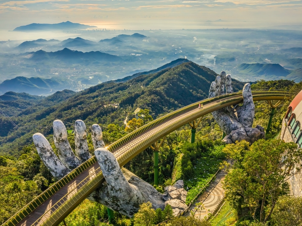 สะพานสีทองที่ได้รับการสนับสนุนจากมือยักษ์บนบานาฮิลส์ ประเทศเวียดนาม โดยมีทิวทัศน์ภูเขาอันงดงามและทิวทัศน์ เที่ยวต่างประเทศงบน้อย เมืองอันห่างไกลเป็นฉากหลัง ซึ่งแตกต่างอย่างน่าอัศจรรย์กับความคึกคักของเมืองพัทยา