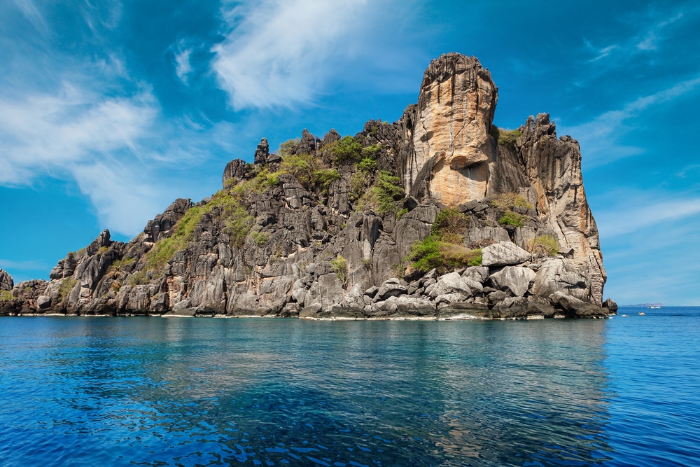 เกาะหินที่มีพืชพรรณกระจัดกระจายโผล่ขึ้นมาจากน้ำทะเลสีฟ้า โดยมีท้องฟ้าสีฟ้าและเมฆเป็นฉากหลัง ทำให้ดูเหมือนเกาะในประเทศไทยในประเทศไทย เกาะที่สวยที่สุดในประเทศไทย