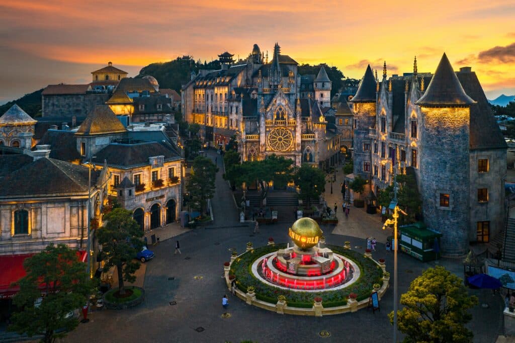 ทัศนียภาพของจัตุรัสเมืองสไตล์ยุโรปยามพระอาทิตย์ตกดิน ซึ่งมีน้ำพุตรง ฮันนีมูน ที่ไหนดี กลางพร้อมลูกโลกสีทอง อาคารประวัติศาสตร์ และท้องฟ้าอันอบอุ่นที่ส่องสว่างด้วยแสงอาทิตย์ตก