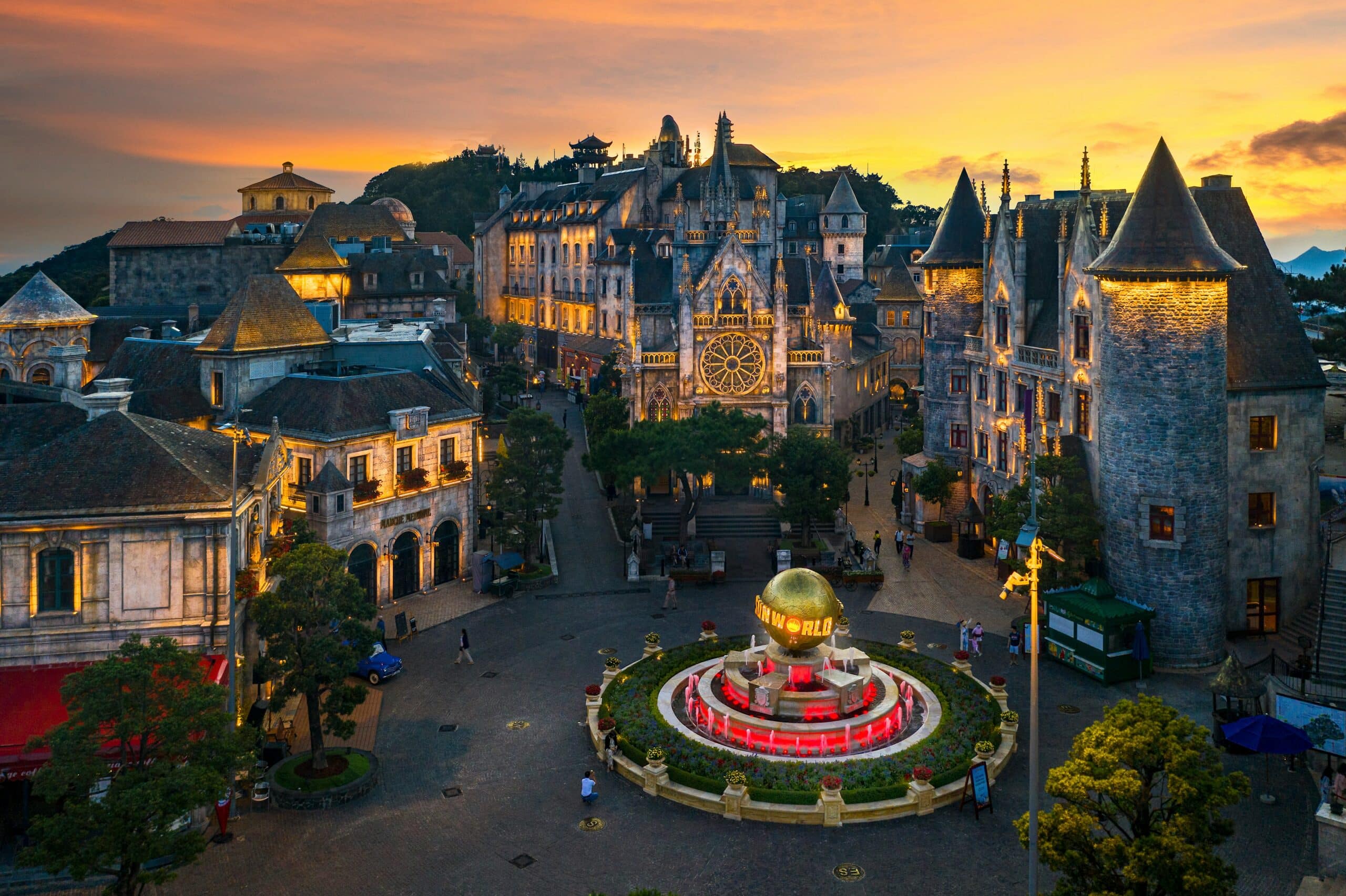 ทัศนียภาพของจัตุรัสเมืองสไตล์ยุโรปยามพระอาทิตย์ตกดิน ซึ่งมีน้ำพุตรงกลางพร้อมลูกโลกสีทอง อาคารประวัติศาสตร์ และท้องฟ้าอันอบอุ่นที่ส่องสว่างด้วยแสงอาทิตย์ตก