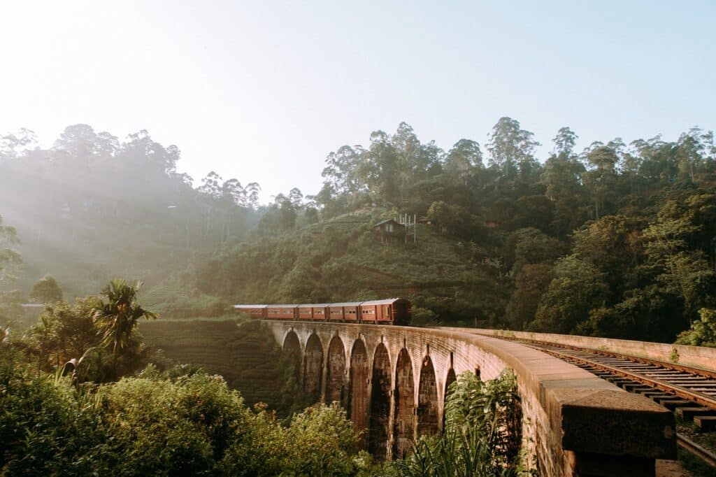 รถไฟวิ่งผ่านสะพานหินที่มีซุ้มโค้งหลายซุ้ม ล้อมรอบด้วยป่าไม้เขียวขจีและเนินเขาในวันที่มีหมอก ฮันนีมูน ที่ไหนดี