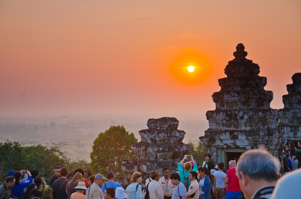 ฝูงชนจำนวนมากมารวมตัวกันที่ ที่เที่ยวกัมพูชา โครงสร้างหินโบราณในประเทศกัมพูชาเพื่อชมพระอาทิตย์ตก โดยมีเส้นขอบฟ้าอาบไปด้วยสีส้ม ทำให้ที่นี่เป็นหนึ่งในสถานที่ที่ต้องไปชมที่เที่ยวกรุงเทพ