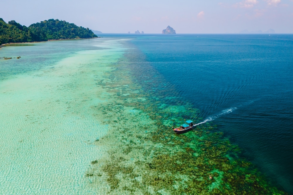 เรือลำเล็กแล่นข้ามผืนน้ำสีฟ้าใส ทะเลใต้สวยๆ ราวกับท้องฟ้าสีฟ้าใกล้ชายฝั่งเขตร้อนอันอุดมสมบูรณ์ พร้อมด้วยหมู่เกาะอันห่างไกลบนขอบฟ้า มอบประสบการณ์หลบหนีที่สมบูรณ์แบบสำหรับผู้ที่ต้องการสำรวจ ที่เที่ยวทะเลใต้