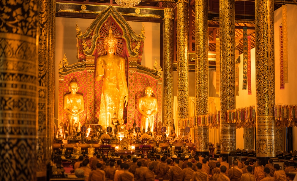 พระพุทธรูปสีทององค์ใหญ่ ล้อมรอบด้วยรูปปั้นขนาดเล็ก และประดับตกแต่งอย่างวิจิตรงดงาม ภายในวัด มีพระสงฆ์นั่งอยู่บนพื้น และทำพิธี สวดมนต์ปีใหม่