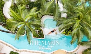 มุมมองทางอากาศของ The Marin Phuket บุคคลกำลังผ่อนคลายในสระว่ายน้ำที่รายล้อมด้วยต้นปาล์มที่โรงแรมเดอะ มาริน ภูเก็ต แสดงให้เห็นบรรยากาศอันเงียบสงบของรีสอร์ต