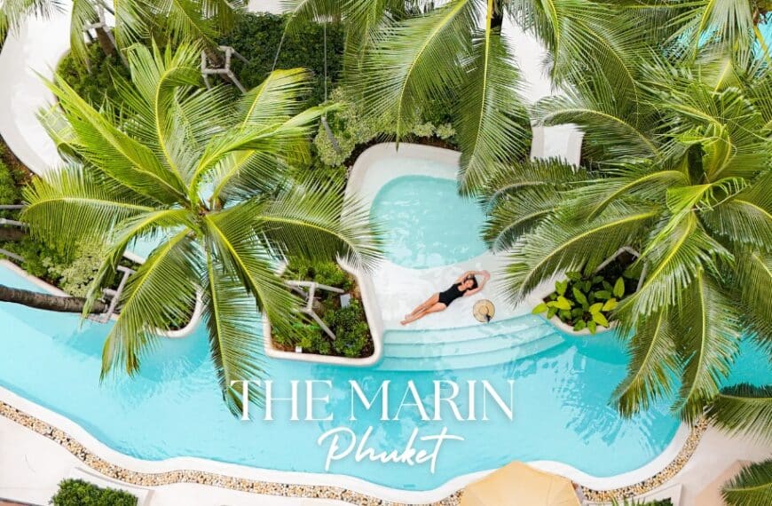 มุมมองทางอากาศของ The Marin Phuket บุคคลกำลังผ่อนคลายในสระว่ายน้ำที่รายล้อมด้วยต้นปาล์มที่โรงแรมเดอะ มาริน ภูเก็ต แสดงให้เห็นบรรยากาศอันเงียบสงบของรีสอร์ต