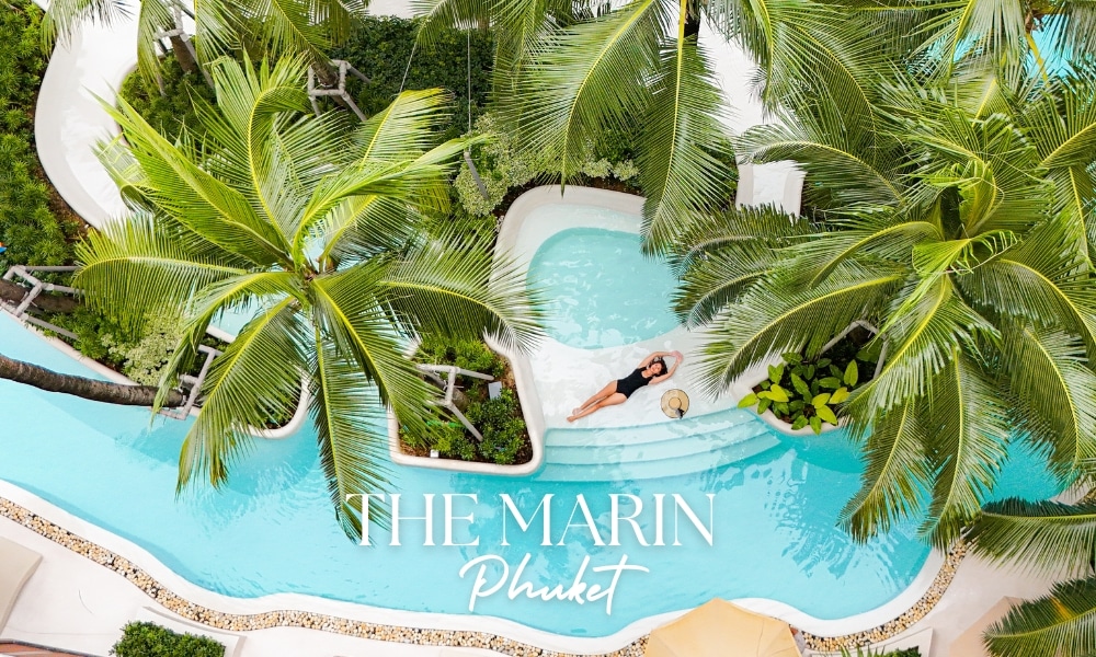 มุมมองทางอากาศของ The Marin Phuket บุคคลกำลังผ่อนคลายในสระว่ายน้ำที่รายล้อมด้วยต้นปาล์มที่โรงแรมเดอะ มาริน ภูเก็ต แสดงให้เห็นบรรยากาศอันเงียบสงบของรีสอร์ต