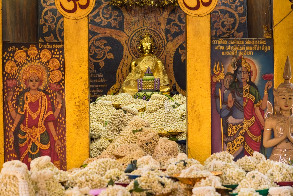 พระพุทธรูปสีทองอร่ามประดับพวงมาลัยดอกไม้นานาพันธุ์ ประดิษฐานอยู่ตรงกลาง ประดิษฐานด้วยภาพวาดรวม พิกัด ไหว้ของานเทพเจ้าสององค์บนฉากหลังสีสันสดใส สร้างบรรยากาศสงบเงียบให้ผู้ศรัทธาได้ไหว้สักการะ