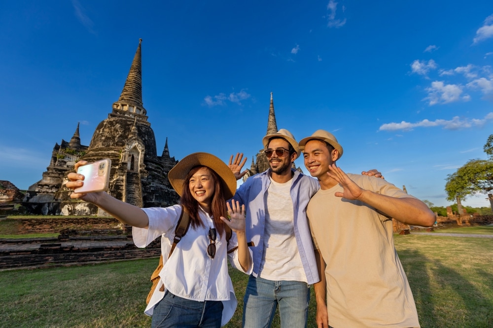 คนสามคนโพสท่าเซลฟี่หน้าซากวัดโบราณใต้ท้องฟ้าสีครามสดใส ท่องเที่ยวอยุธยา เก็บภาพความงามของที่ท่องเที่ยวอยุธยา