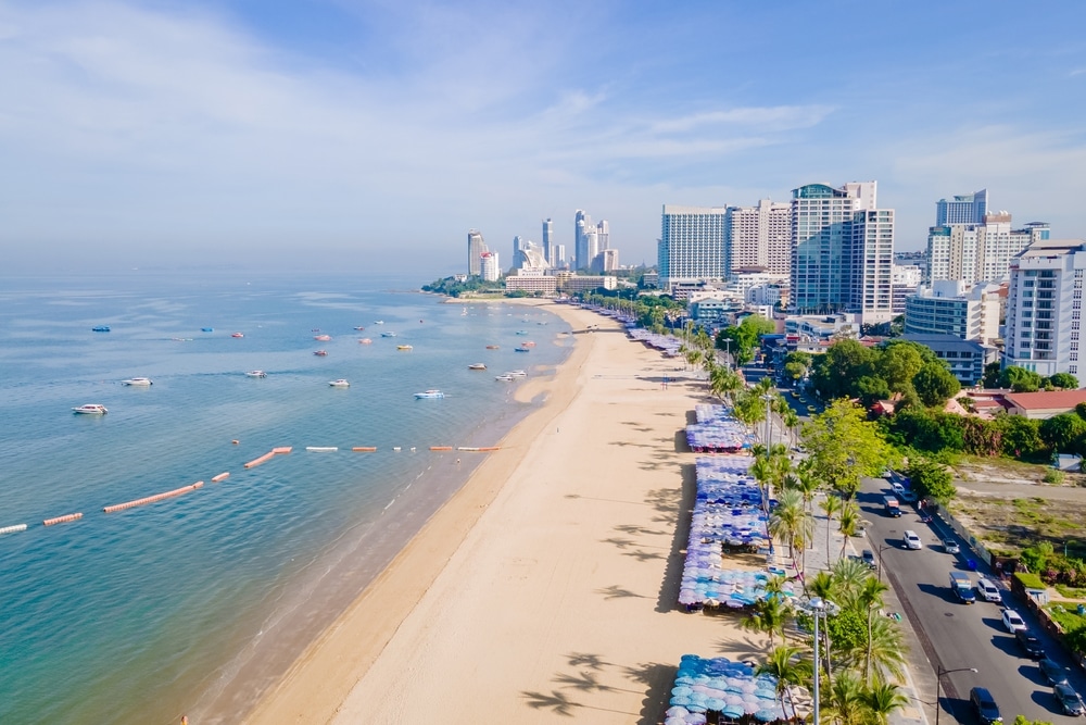 วิวทางอากาศของชายหาดในเมืองที่มีอาคารสูงหลายหลังตามแนวชายฝั่งและเรืออยู่ในน้ำ หาดทรายที่มักเที่ยวหน้าฝนโรแมนติกมักจะว่างเปล่าภายใต้ท้องฟ้าสีครามสดใส ที่เที่ยวครอบครัว