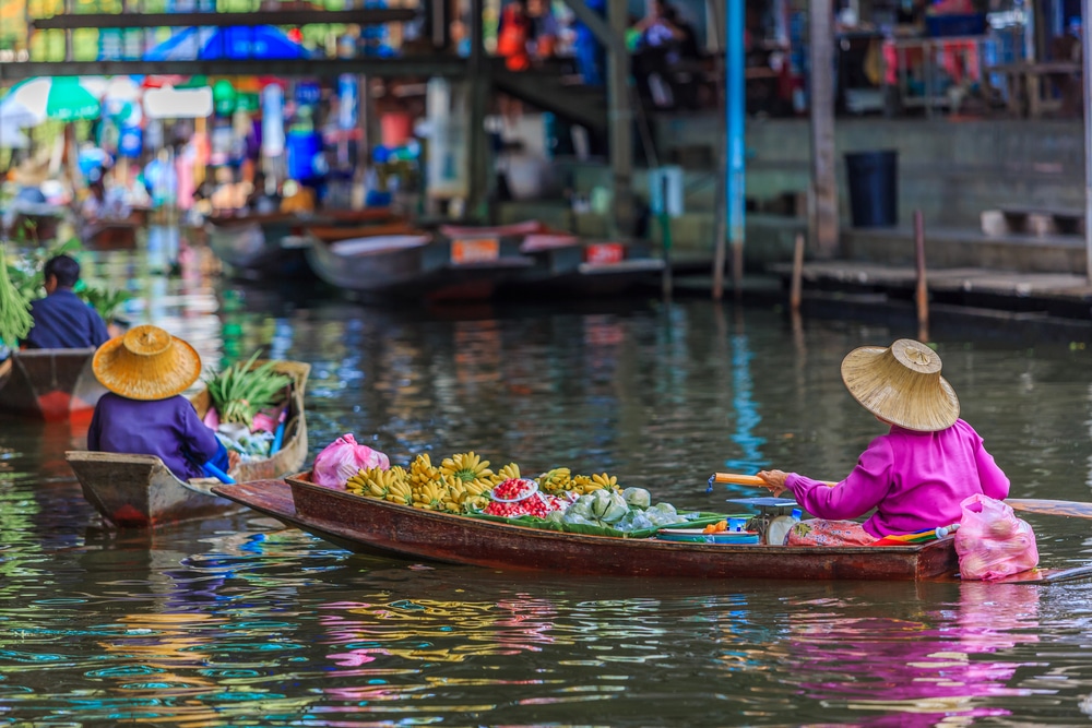 พ่อค้าแม่ค้าที่สวมหมวกแบบดั้งเดิมจะขายผลไม้และสินค้าจากเรือในตลาดริมคลองที่พลุกพล่าน ท่องเที่ยวเมืองรอง ชวนเพื่อน ช ให้นักท่องเที่ยวได้สัมผัสประสบการณ์การท่องเที่ยวเมืองรองที่แท้จริง