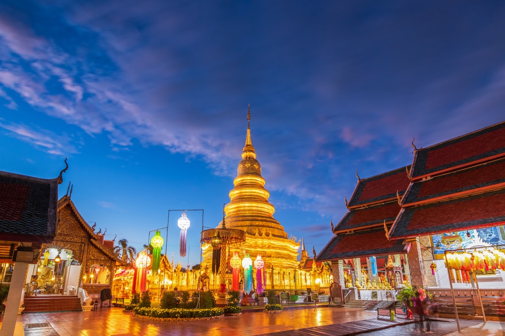 เจดีย์สีทองอร่ามที่ส่องสว่างและอาคาร วัดพระธาตุหริภุญชัย รอบ ๆ วัดภายใต้ท้องฟ้ายามพลบค่ำ วัดพระธาตุหริภุญชัยวรมหาวิหาร