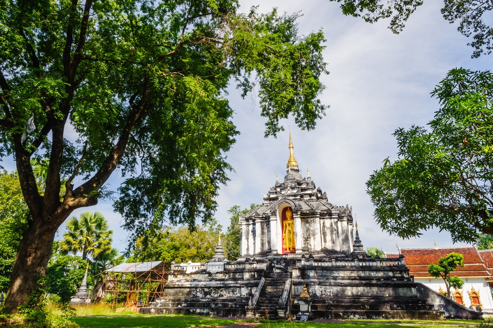 วัดประวัติศาสตร์ที่มีพระพุทธรูปทองคำตั้งอยู่ท่ามกลางต้นไม้สีเขียวภายใต้ท้องฟ้า ท่องเที่ยวจังหวัดลำพูน สีฟ้า