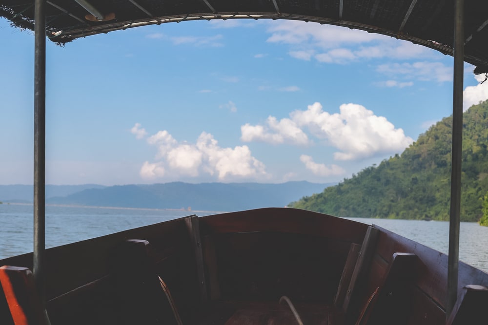 มุมมองจากภายในเรือในทะเลสาบในพื้นที่ท่องเที่ยวจังหวัดลำพูน ท้องฟ้าสีฟ้าใส เมฆกระจัดกระจาย และทิวเขาเขียวขจีเป็นฉากหลัง ท่องเที่ยวกรุงเทพ