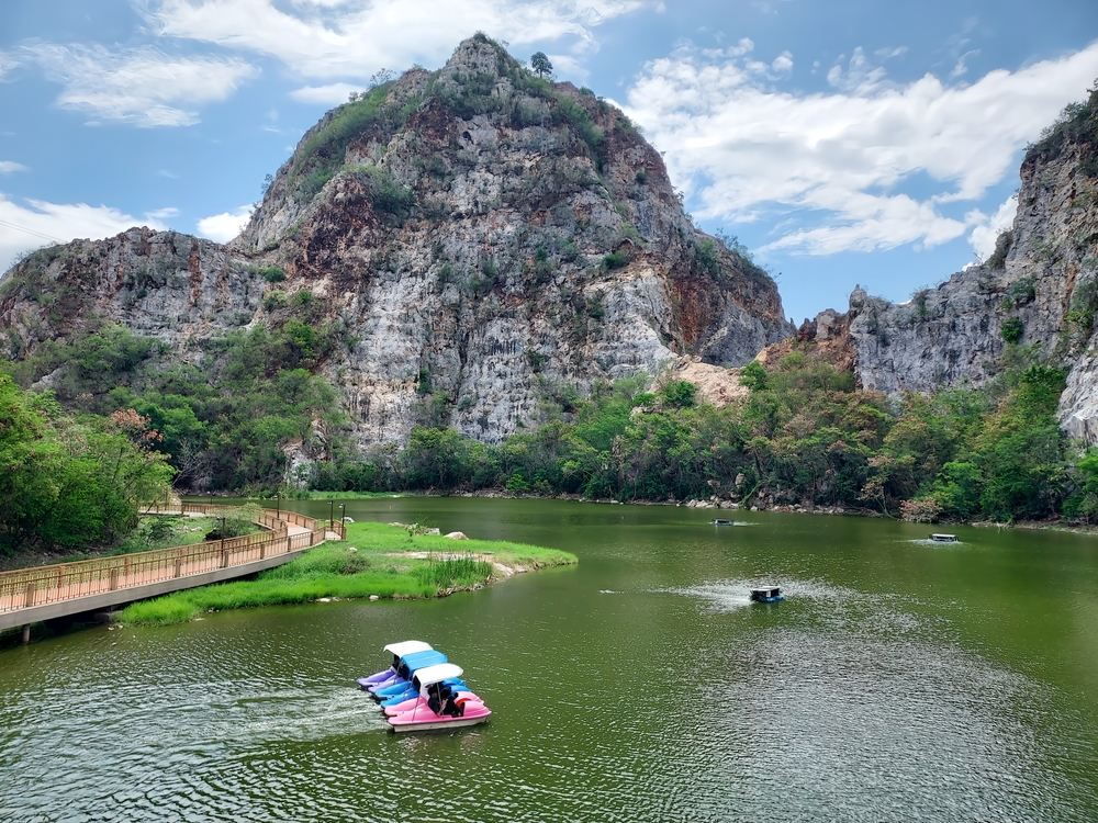 อุทยานที่มีทัศนียภาพสวยงามเป็นจุดเด่นของการท่องเที่ยวลำพูน มีลักษณะเป็นเนินเขาหินและทะเลสาบที่มีเรือถีบหลายลำล่องไปมาบนผิวน้ำภายใต้ ท่องเที่ยวราชบุรี ท้องฟ้าที่มีเมฆบางส่วน มีเส้นทางเดินเลียบไปตามริมทะเลสาบอย่างช้าๆ