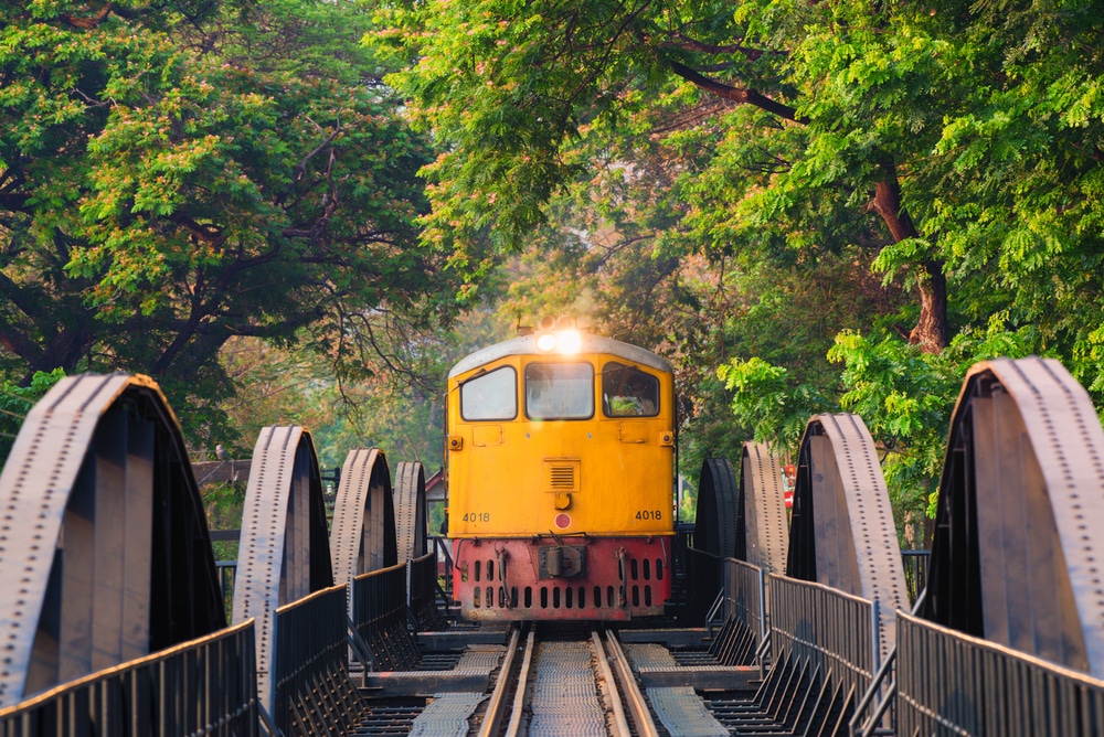 รถไฟสีเหลืองข้ามสะพานเหล็กที่รายล้อมไปด้วยต้นไม้สีเขียวชอุ่ม มอบประสบการณ์ที่เที่ยวหน้าฝนโรแมนติก ที่เที่ยวสำหรับครอบครัว ที่เที่ยวสำหรับครอบครัว