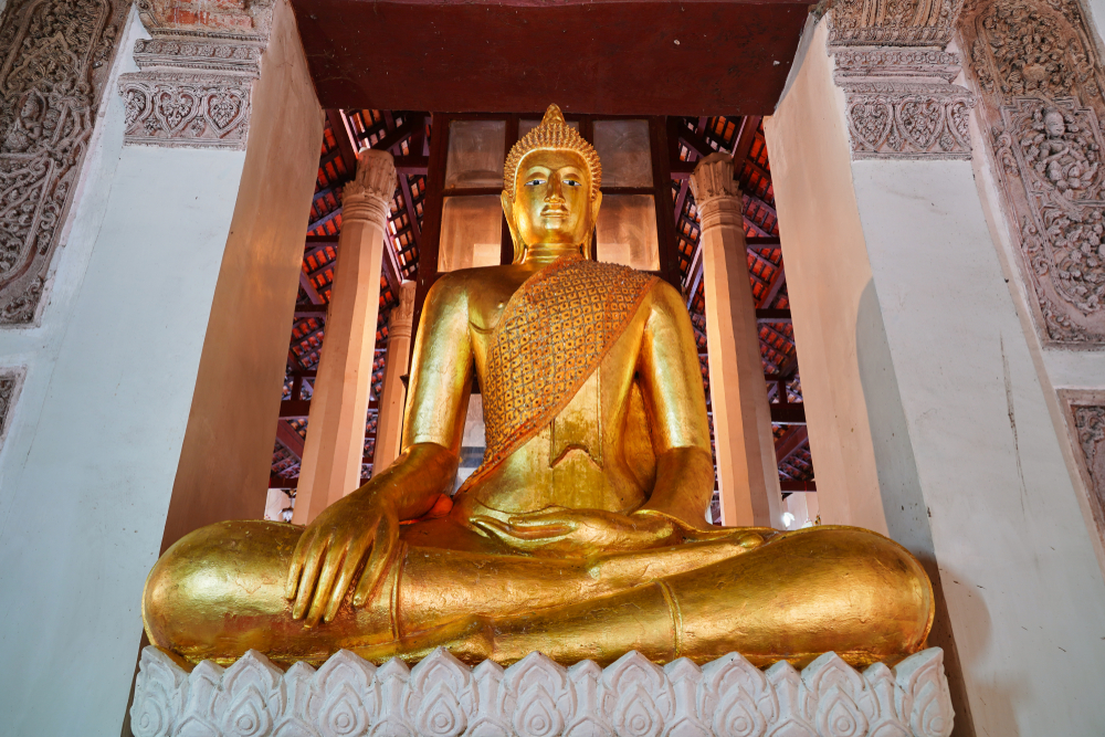 พระพุทธรูปทองคำขนาดใหญ่นั่งขัดสมาธิในวัด ล้อมรอบด้วยงานแกะสลักอันวิจิตรงดงาม เป็นตัวอย่างที่ชัดเจนของความงามอันเงียบสงบที่มักพบใน วัดที่ลพบุรี