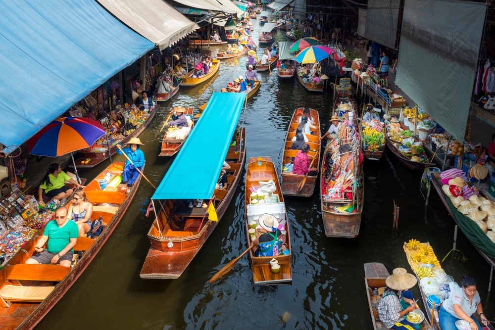 ภาพมุมสูง ตลาดน้ำกรุงเทพ แสดงให้เห็นบรรยากาศคึกคักของตลาดน้ำกรุงเทพ ซึ่งเรือบรรทุกผลไม้ ผัก และสินค้ามากมายล่องไปตามลำน้ำแคบๆ พ่อค้าแม่ค้าและนักช้อปเดินเตร่ไปมาในตลาดที่คึกคัก ท่ามกลางร่มและผ้าใบสีสันสดใส