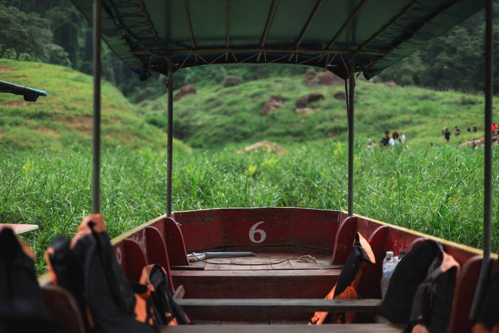 จากภายในเรือที่เปิดโล่ง ใต้ร่มไม้สีเขียวสดใส คุณจะได้รับการต้อนรับ ท่องเที่ยวภาคกลาง ด้วยทิวทัศน์อันน่าหลงใหลของเนินเขาสีเขียวชอุ่มและบุคคลที่อยู่ห่างไกล เป็นฉากที่เหมาะสำหรับผู้ที่กำลังมองหาสถานที่ท่องเที่ยวหน้าฝนใกล้กรุงเทพที่หลีกหนีความวุ่นวาย