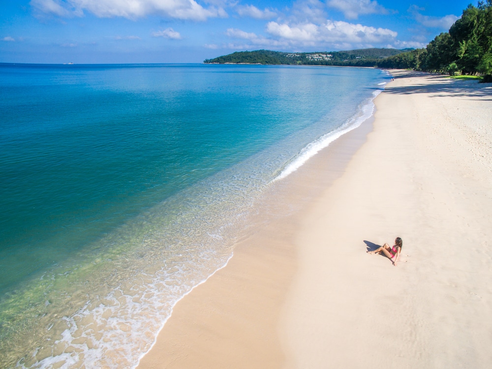 มุมมองทางอากาศของ ทะเลภูเก็ต ชายหาดภูเก็ตที่รกร้างว่างเปล่า น้ำทะเลสีฟ้าใสและเมฆบางๆ คนๆ หนึ่งกำลังพักผ่อนบนผืนทรายใกล้ชายฝั่ง