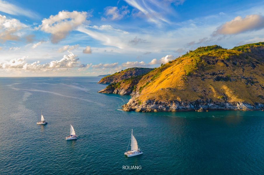 ภาพ ท่องเที่ยวภาคใต้ ถ่ายทางอากาศของเรือใบ 3 ลำ แนวชายฝั่งโขดหินตามแนวไหล่เขาภาคใต้ ใต้ท้องฟ้ามีเมฆเป็นบางส่วน เหมาะสำหรับท่องเที่ยวภาคใต้