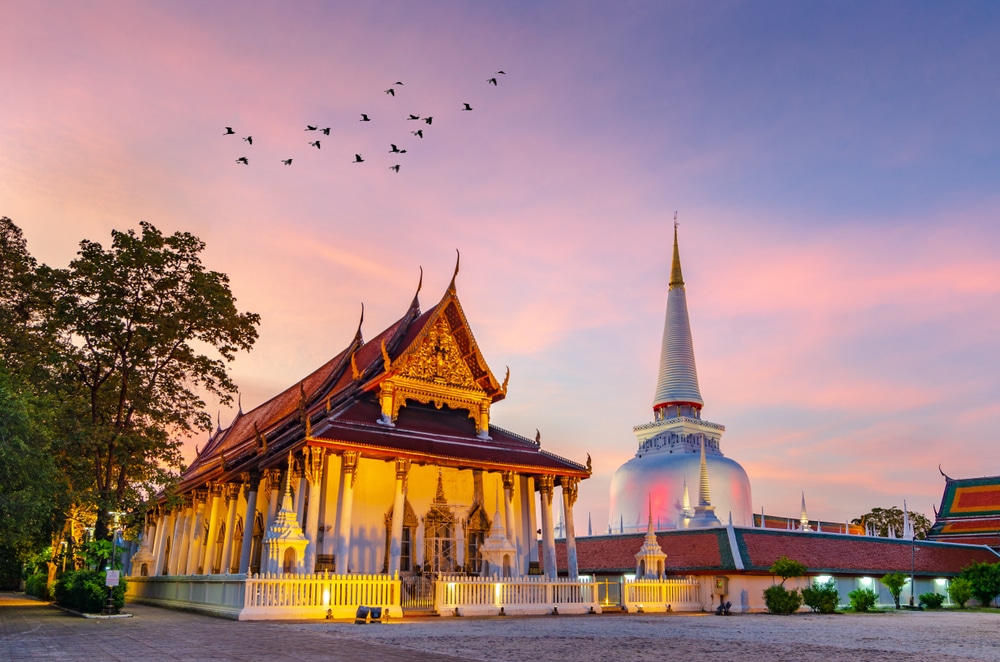 วัดที่มี วัดที่สวยที่สุดในประเทศไทย หลังคาสวยงามและเจดีย์สีขาวสูงตระหง่านรับกับแสงสีทองของพระอาทิตย์ตกดิน พร้อมทั้งนกที่บินอย่างสง่างามบนท้องฟ้า ท่ามกลางความเงียบสงบของวัดพระนอน.