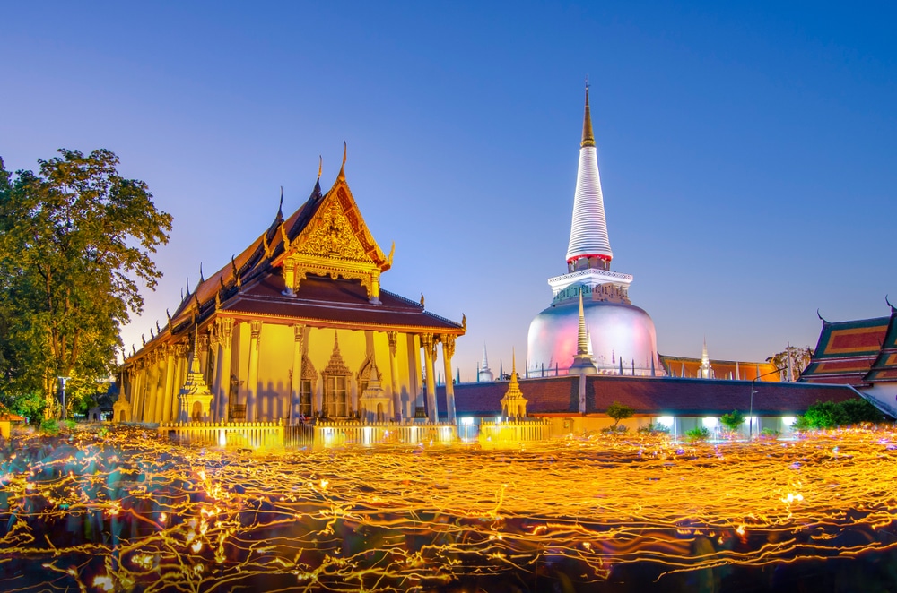 ทัศนียภาพ วัดที่สวยที่สุดในประเทศไทย ยามค่ำคืนอันเงียบสงบของวัดพระนอน ซึ่งมีเจดีย์ที่ประดับไฟอย่างสง่างาม รายล้อมไปด้วยแสงเทียนที่ส่องสว่างอ่อนๆ จากขบวนแห่.