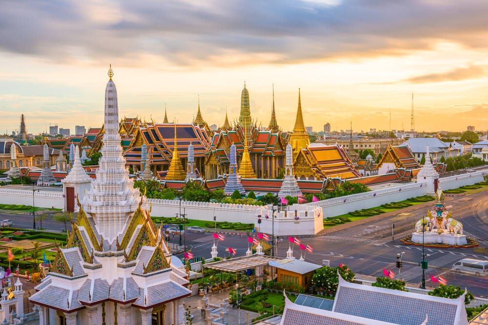 ภาพมุมสูงแสดงให้เห็น วัดที่สวยที่สุดในประเทศไทย วัดพระนอนอันสง่างามที่มีหลังคาและยอดแหลมที่ตั้งตระหง่านท่ามกลางทัศนียภาพของเมืองภายใต้ท้องฟ้าที่มีเมฆมากขณะพระอาทิตย์ตกดิน.