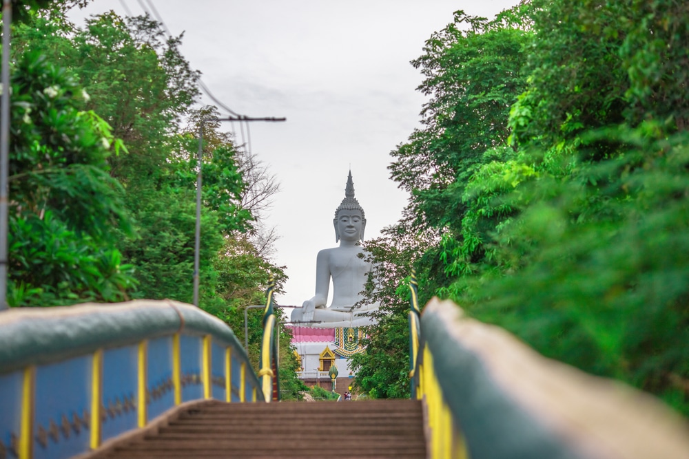 ขั้นบันได รอยพระพุทธบาท นำไปสู่พระพุทธรูปสีขาวขนาดใหญ่ ชวนให้นึกถึง รอยพระพุทธบาท ล้อมรอบด้วยต้นไม้เขียวชอุ่ม