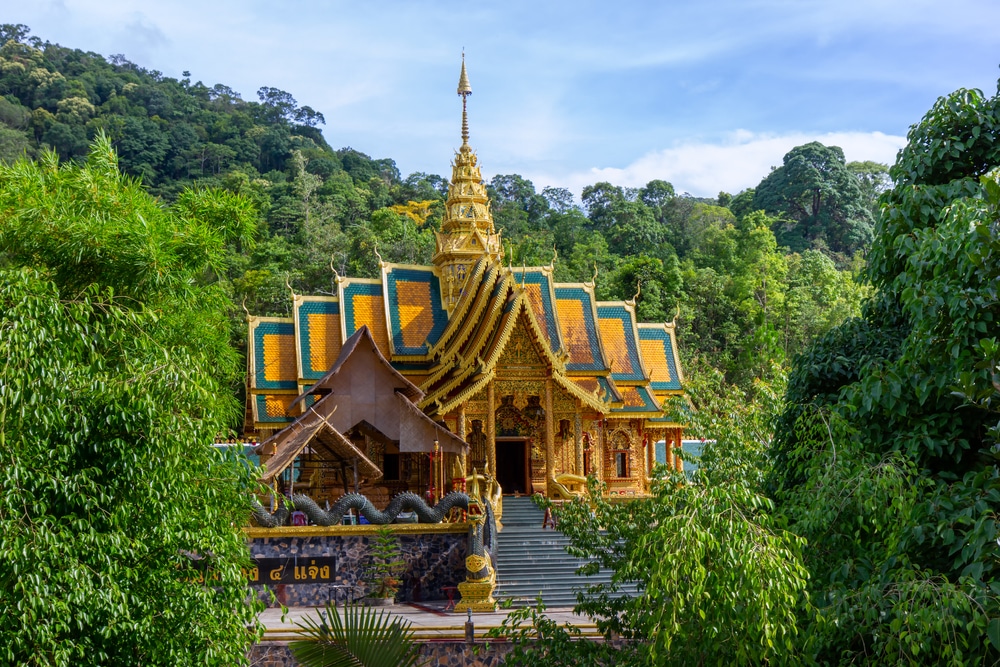 วัด รอยพระพุทธบาท สีทองชวนให้นึกถึงรอยพระพุทธบาท ล้อมรอบด้วยต้นไม้สีเขียวชอุ่ม โดยมีภูเขาเป็นฉากหลังภายใต้ท้องฟ้าสีฟ้าใส