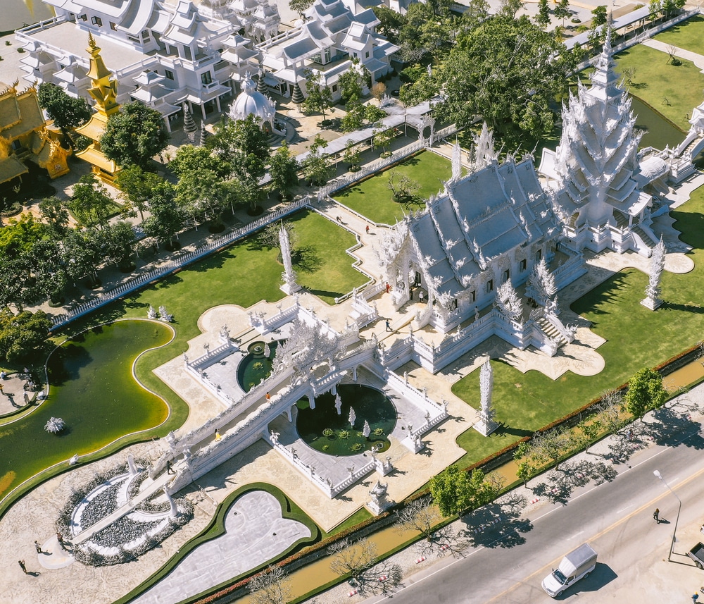 มุมมองทางอากาศของวัดพระนอน ซึ่งเป็นวัดสีขาวที่มีการออกแบบที่ วัดที่สวยที่สุดในประเทศไทย ประณีต ล้อมรอบด้วยต้นไม้เขียวขจีและบ่อน้ำ ติดถนน เหมาะสำหรับผู้แสวงหาประสบการณ์อันเงียบสงบของการไหว้พระนอน.