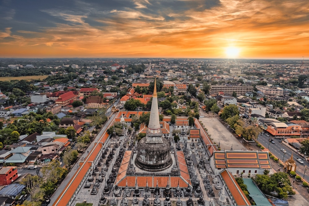 มุมมองทางอากาศของกลุ่มวัดพระ วัดที่สวยที่สุดในประเทศไทย นอนโบราณที่มีเจดีย์ตรงกลางล้อมรอบด้วยรูปปั้นต่างๆ มากมาย โดยมีฉากหลังเป็นพระอาทิตย์ตกที่สวยงามและทิวทัศน์ของเมือง.