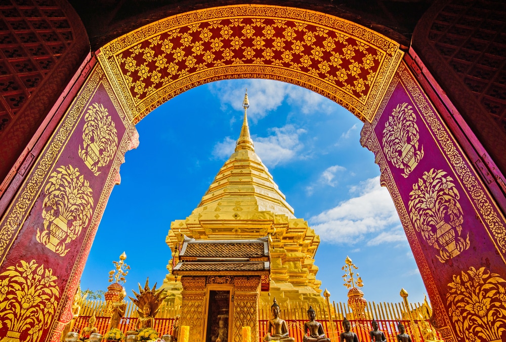 ทัศนียภาพอันสวยงามตระการตา วัดที่สวยที่สุดในประเทศไทย ของวัดพระนอนเผยให้เห็นซุ้มประตูสีแดงและสีทองอันวิจิตรบรรจงที่ล้อมยอดแหลมสีทองไว้อย่างงดงามท่ามกลางท้องฟ้าสีฟ้าใส เชื้อเชิญให้ผู้มาเยือนทุกคนมาสัมผัสกับความงามอันเงียบสงบของที่นี่.