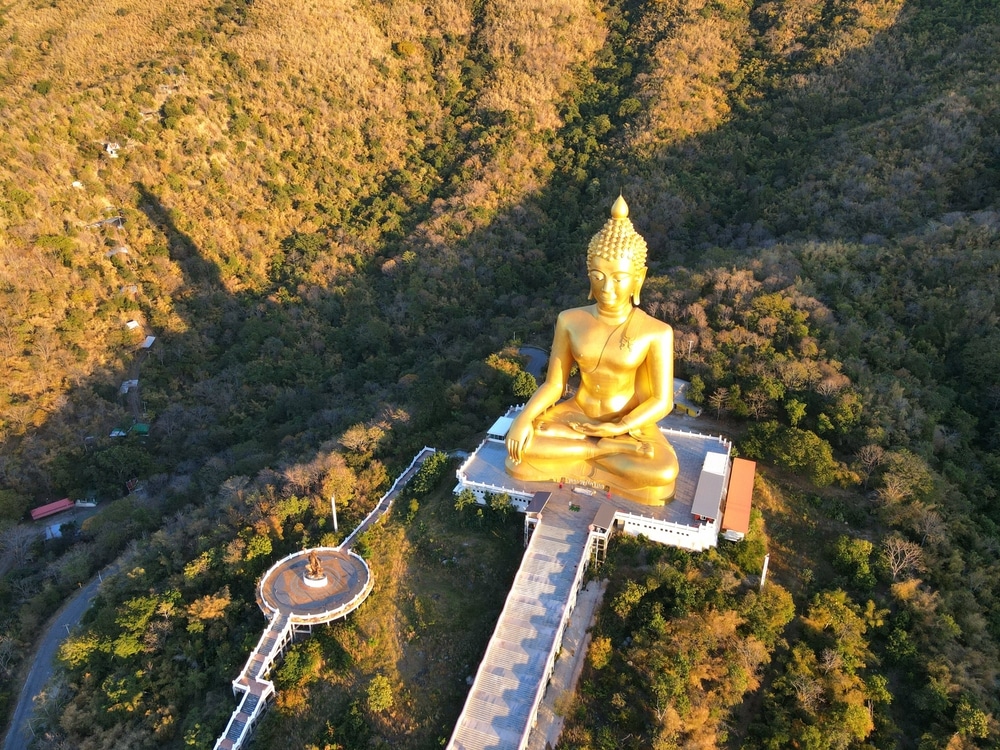 มุมมองทาง รอยพระพุทธบาท อากาศของพระพุทธรูปทองคำขนาดใหญ่ในท่านั่ง มองเห็นรอยพระพุทธบาท ท่ามกลางเนินเขาเขียวขจี มีทางเดินที่สวยงามทอดไปสู่พระพุทธรูป