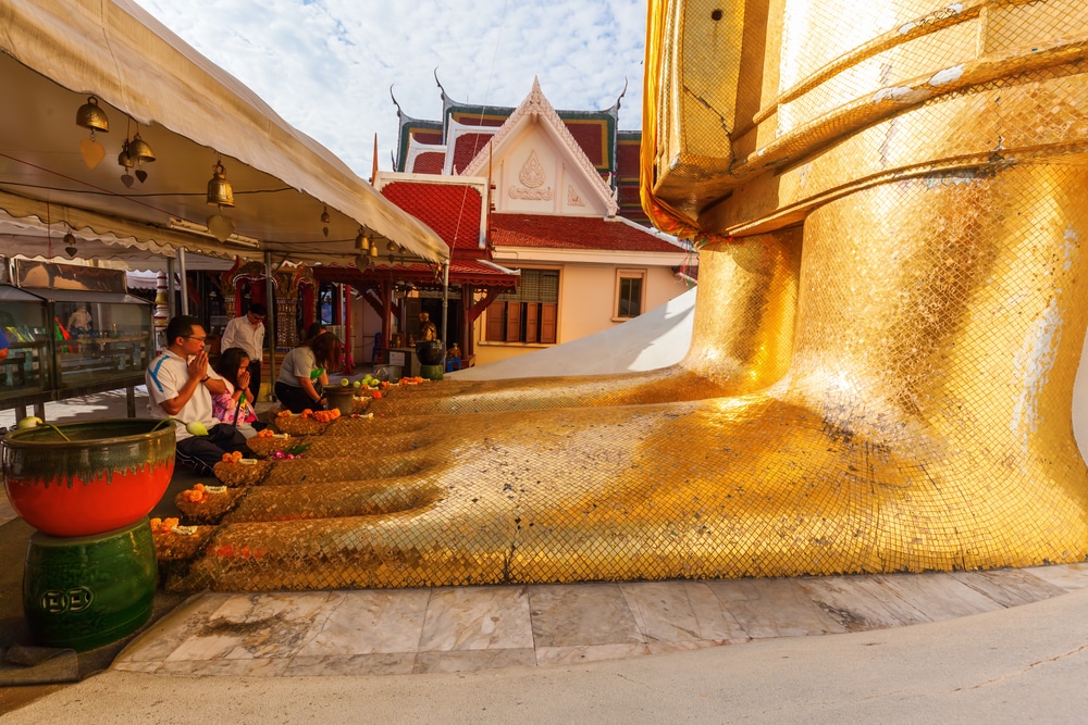 นักท่องเที่ยวนั่งสวดมนต์ข้าง รอยพระพุทธบาท พระบาททองคำของพระพุทธไสยาสน์ขนาดใหญ่ที่วัดโพธิ์ในกรุงเทพฯ สะท้อนถึงความสำคัญอันเงียบสงบของรอยพระพุทธบาท