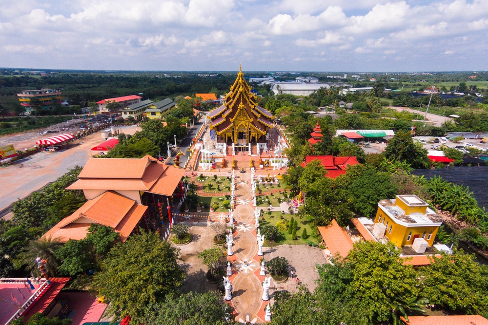 มุมมองทางอากาศของวัดพระนอน ซึ่ง วัดที่สวยที่สุดในประเทศไทย เป็นกลุ่มวัดขนาดใหญ่ มีสถาปัตยกรรมวิจิตรงดงาม ล้อมรอบด้วยต้นไม้และอาคารอื่นๆ ภายใต้ท้องฟ้าที่มีเมฆบางส่วน.