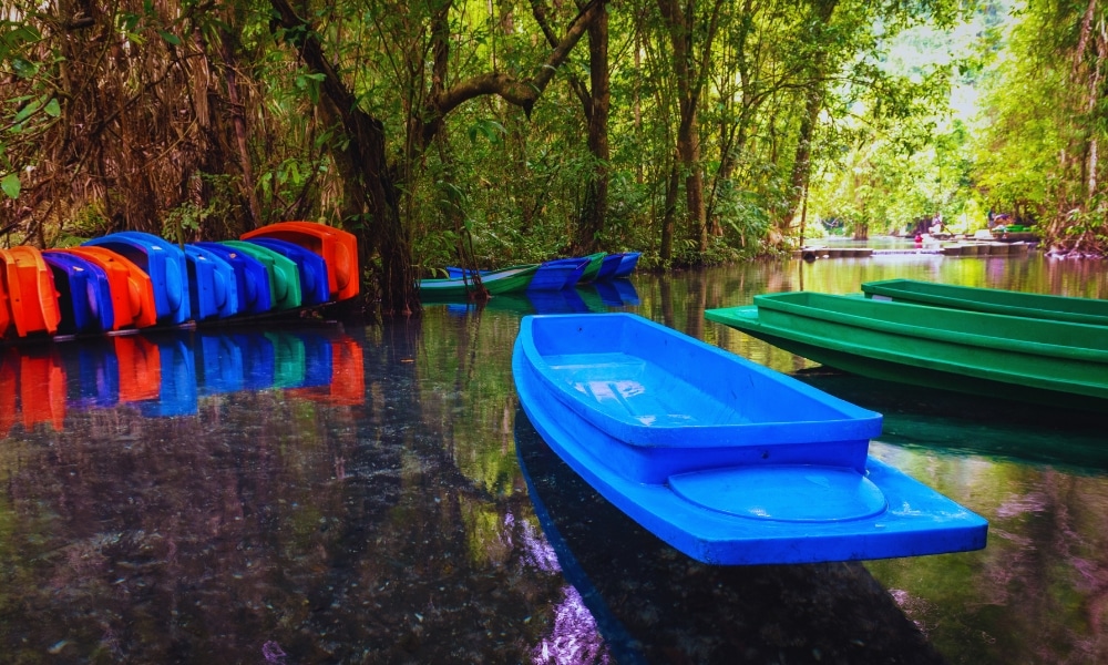 เรือคายัคและเรือสีสันสดใสจอด ที่เที่ยวตรัง เทียบท่าอยู่ในแม่น้ำอันเงียบสงบและใสซึ่งล้อมรอบด้วยป่าไม้เขียวชอุ่ม ทำให้ที่นี่เป็นหนึ่งในสถานที่ท่องเที่ยวจังหวัดชุมพรที่เงียบสงบที่สุด.