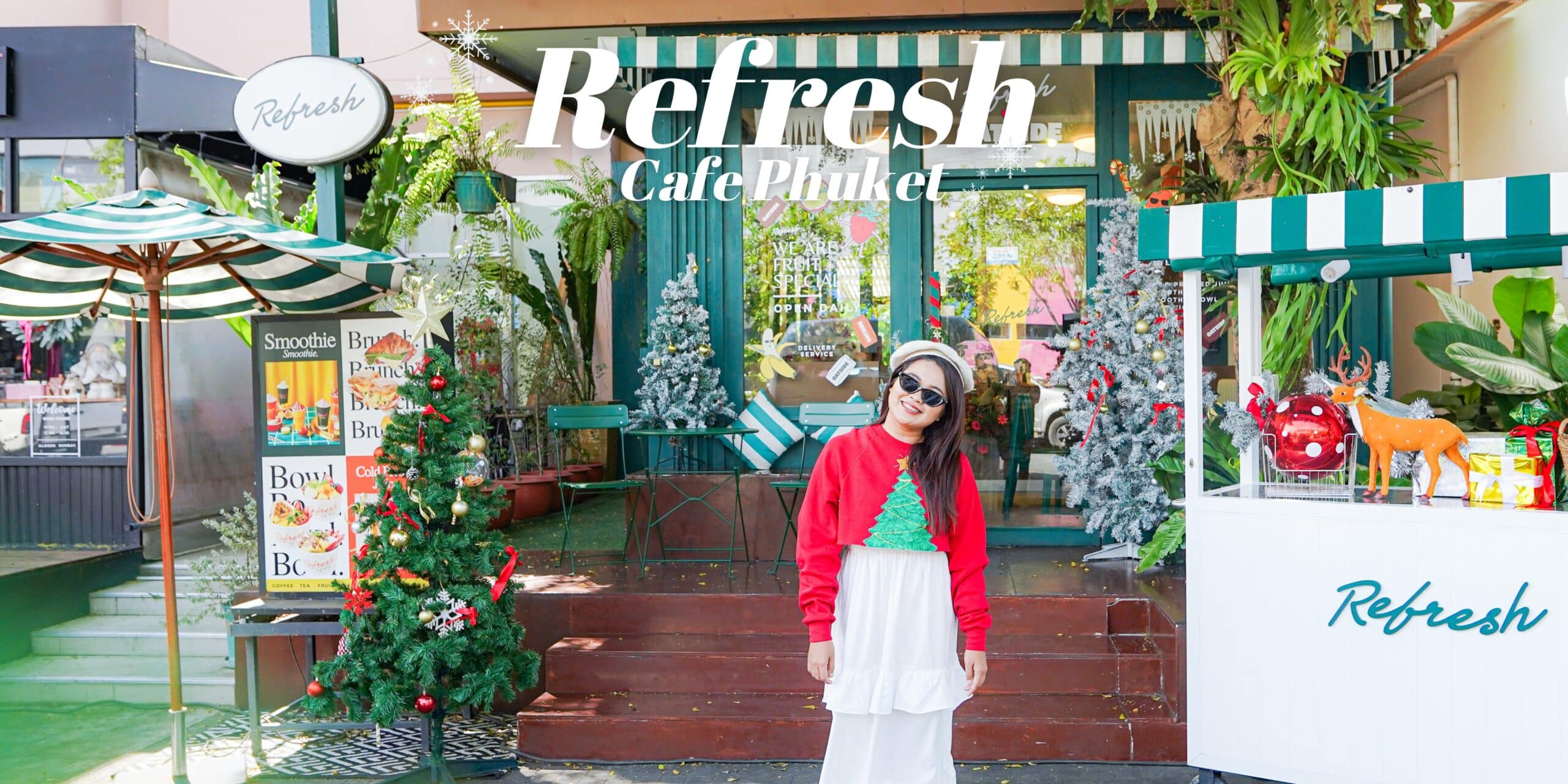 ผู้ที่สวมชุดเฉลิมฉลองยืนอยู่หน้า Refresh Cafe Phuket คาเฟ่บรรยากาศสบายๆ ในใจกลางเมืองภูเก็ต ล้อมรอบด้วยต้นไม้ที่ตกแต่งอย่างสวยงามและของประดับตกแต่งคริสต์มาส ถือเป็นการกลับมาอีกครั้งในฤดูกาลอันน่ารื่นรมย์.