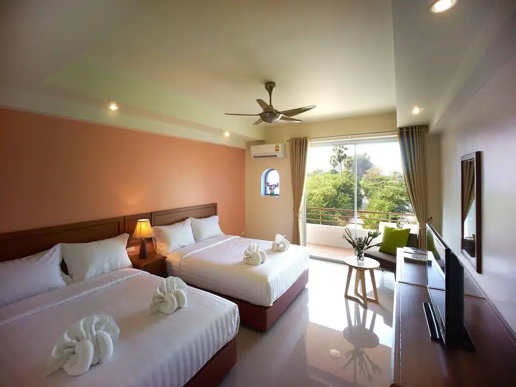 สัมผัสความสะดวกสบายในห้องพัก ที่พักหาดเจ้าหลาว อันเงียบสงบของโรงแรมพร้อมเตียงคู่ 2 เตียง ตกแต่งด้วยผ้าปูที่นอนสีขาวและรูปปั้นผ้าเช็ดตัว เพลิดเพลินกับสิ่งอำนวยความสะดวก เช่น ทีวี โต๊ะไม้ โคมไฟ และเก้าอี้เท้าแขน หน้าต่างมองเห็นวิวแมกไม้เขียวขจี เหมาะสำหรับการพักผ่อนครั้งต่อไปที่หาดเจ้าหลาวติดทะเล.