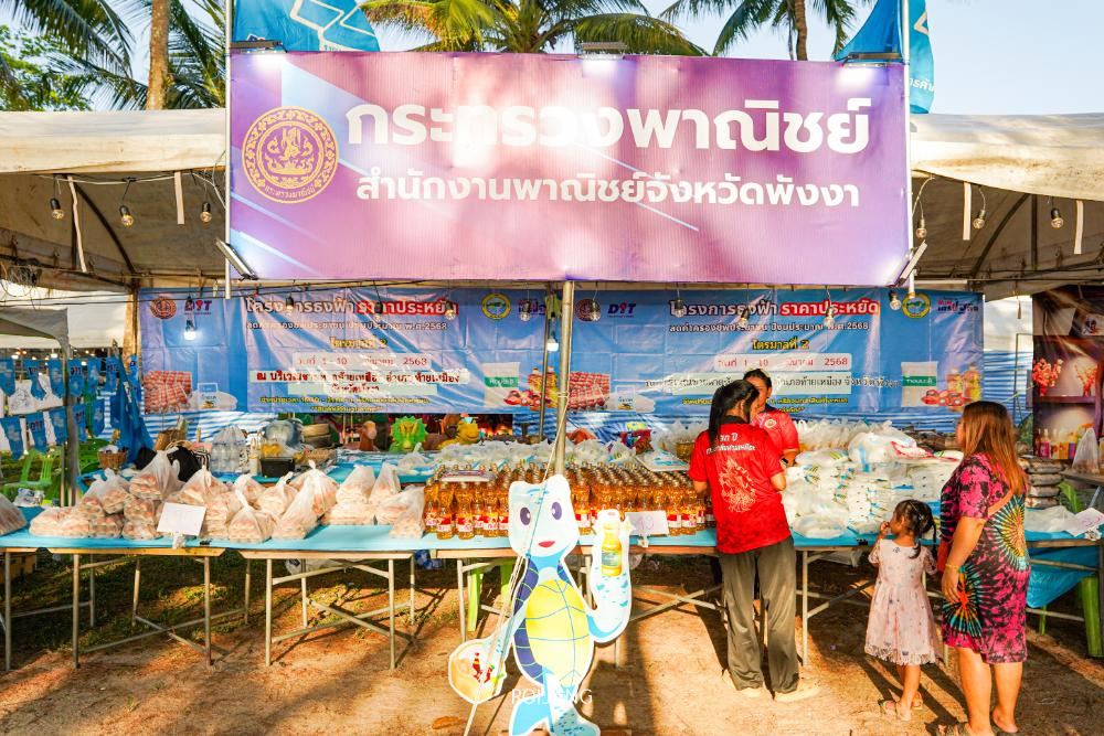 แผงขายของในตลาดที่ประดับด้วยป้ายภาษาไทยจะแสดงสินค้าบรรจุหีบห่อมากมาย ใกล้ๆ กันมีรูปหมีตัดเป็นรูปการ์ตูนเพิ่มความแปลกตาเมื่อผู้มาเยือนสำรวจข้อเสนอต่างๆ ชวนให้นึกถึงงานปล่อยเต่ารักษา 2568 ซึ่งเป็นจิตวิญญาณแห่งความรื่นเริง.