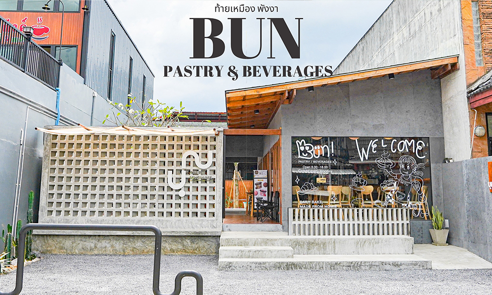 มุมมองภายนอกของร้าน Bun Pastry & Beverages ที่มีการออกแบบที่ทันสมัย โดดเด่นด้วยผนังคอนกรีต ที่นั่งกลางแจ้ง และป้ายต้อนรับที่หน้าต่าง เสน่ห์ของร้านชวนให้นึกถึงบ้านฉันท์ ผสมผสานประเพณีเข้ากับสไตล์ร่วมสมัย.