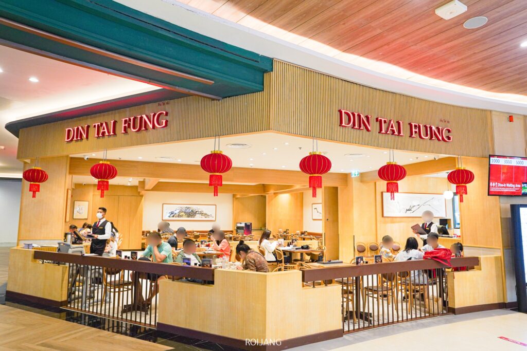 บรรยากาศภายในร้านอาหาร Din Tai Fung ภูเก็ต ที่มีลูกค้านั่งรับประทานอาหารอยู่ โคมไฟสีแดงห้อยระย้าอย่างสง่างามตามภายนอกร้าน สาดแสงอบอุ่นให้สวรรค์แห่งการรับประทานอาหารแห่งนี้.