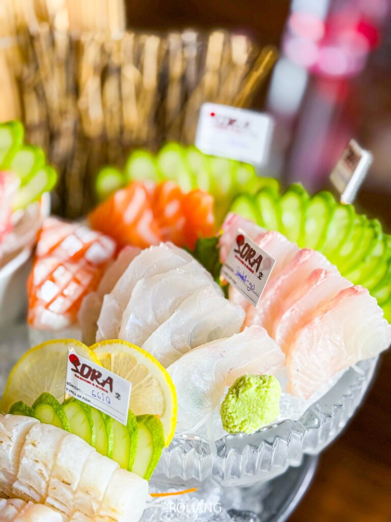 Sora Sashimi นำเสนอซาซิมิชิ้นต่างๆ ที่ยอดเยี่ยมหลากหลายชนิด ไม่ว่าจะเป็นปลาแซลมอนและปลาน้ำจืด จัดเรียงอย่างประณีตด้วยแตงกวา มะนาวฝาน และวาซาบิบนจานที่เต็มไปด้วยน้ำแข็ง.