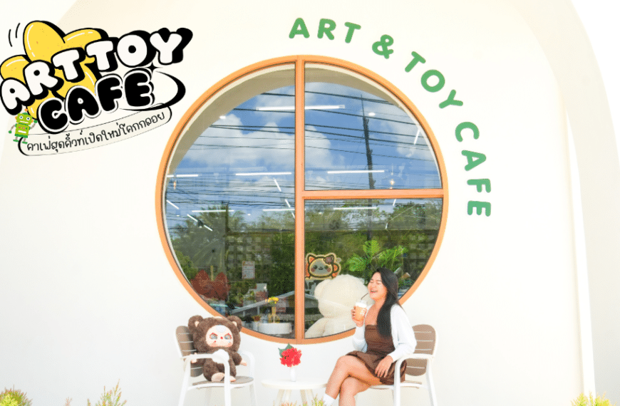 ด้านนอกของร้าน Art & Toy Cafe Phangnga ที่น่ารัก มีหญิงสาวคนหนึ่งกำลังนั่งจิบเครื่องดื่มพร้อมของเล่นแปลก ๆ ที่วางอยู่บนเก้าอี้ โลโก้ของร้านช่วยเพิ่มบรรยากาศที่แสนสนุกให้กับบรรยากาศอันเงียบสงบแห่งนี้.